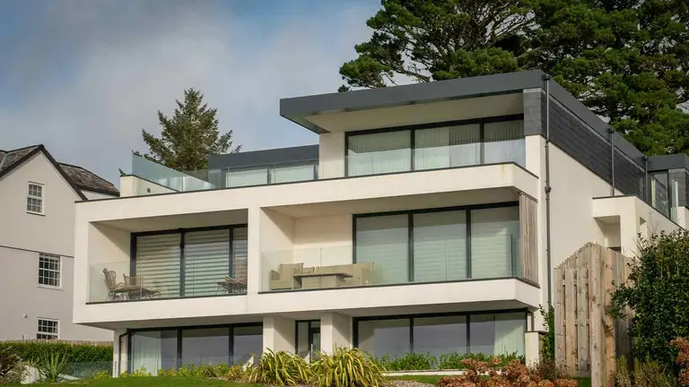 A modern white three-storey house with glass-railed balconies stepping down a coastal slope, the kind of high-value marital home where entirety protection is worth establishing precisely